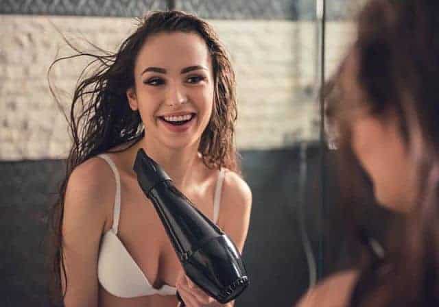 A beautiful girl blow-drying freshly shampooed hair