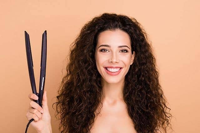 A cute curly girl holding the steam flat iron