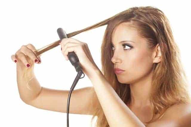 A girl straightening the section of the hair with a flat iron 