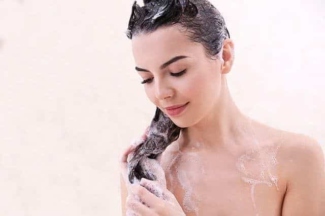 a beautiful young woman washing her hair with ph balanced shampoo