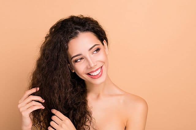 Charming curly haired girl applying keratin oil