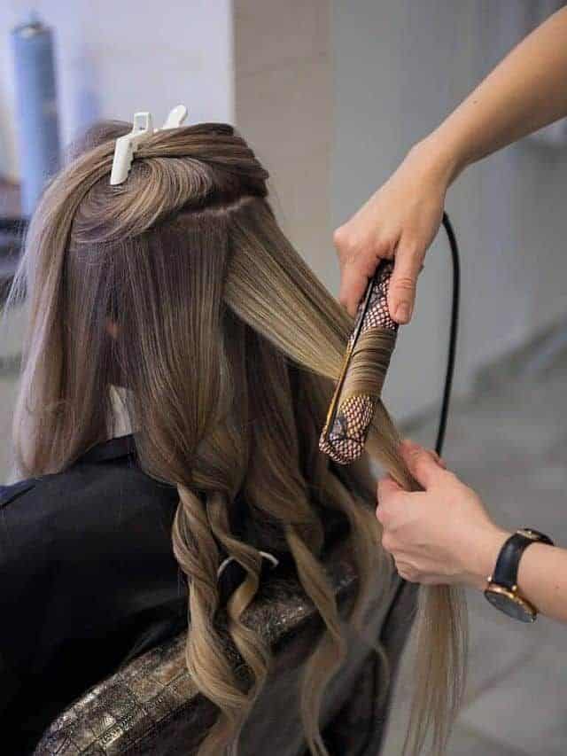 Hair stylist uses hair straightener and curler to style client's hair