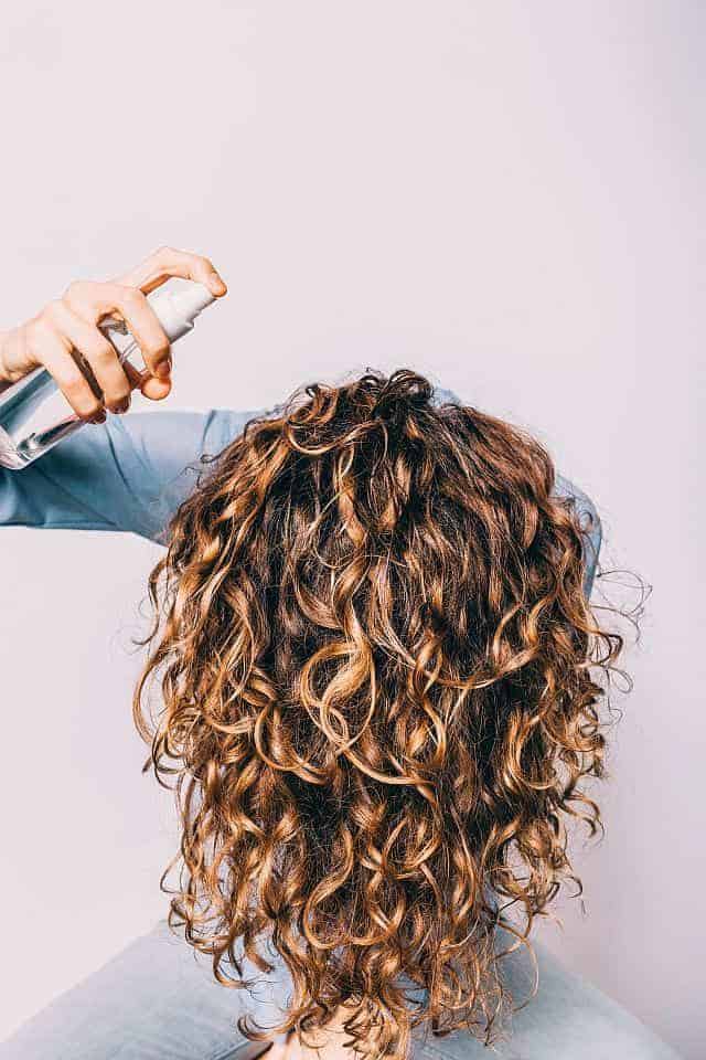 a girl applying sea salt spray to her curly hair