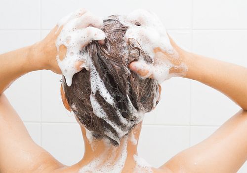 a woman washing her hair with a scalp exfoliating shampoo