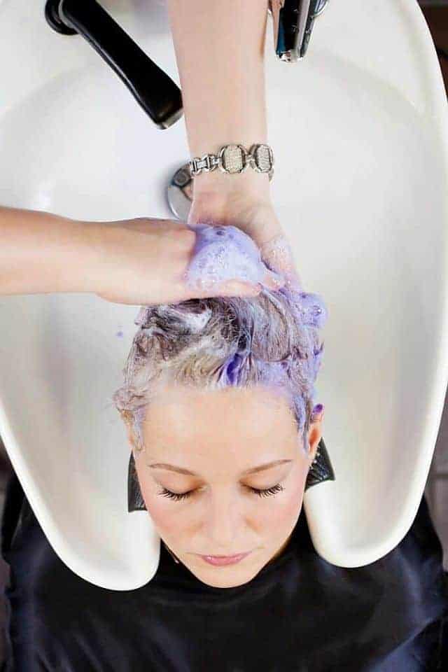 hairdresser uses purple shampoo to wash client's hair