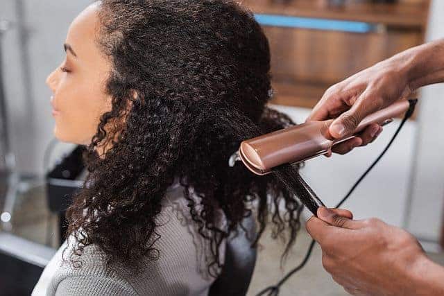 hairdresser using a titanium hair straightener on unruly hair