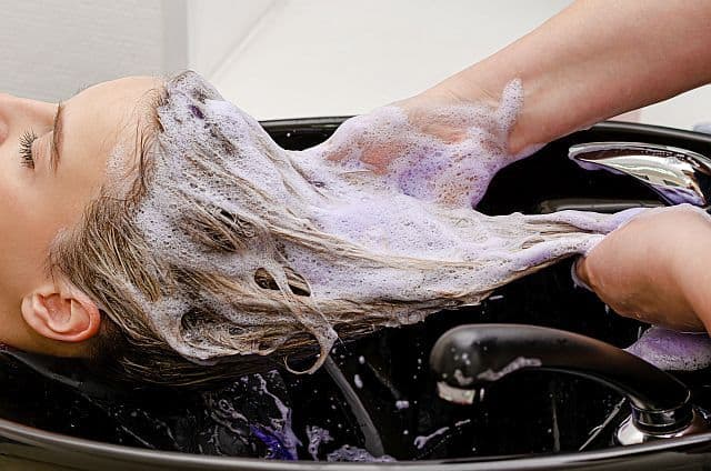 hairdresser washing hair with purple shampoo in the salon
