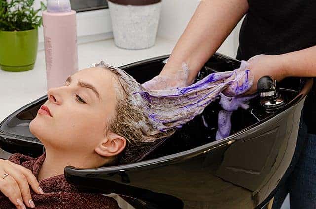 hairstylist washing clients' hair with a purple shampoo