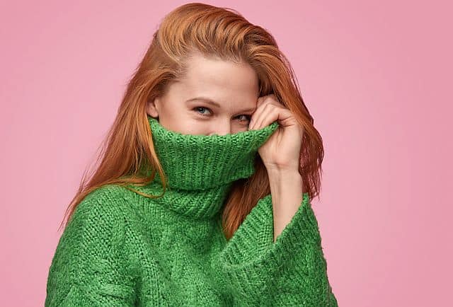 Smiling girl with red hair covering her mouth with the sweater