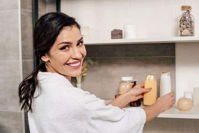 a smiling woman in the bathroom holding a shampoo bottle