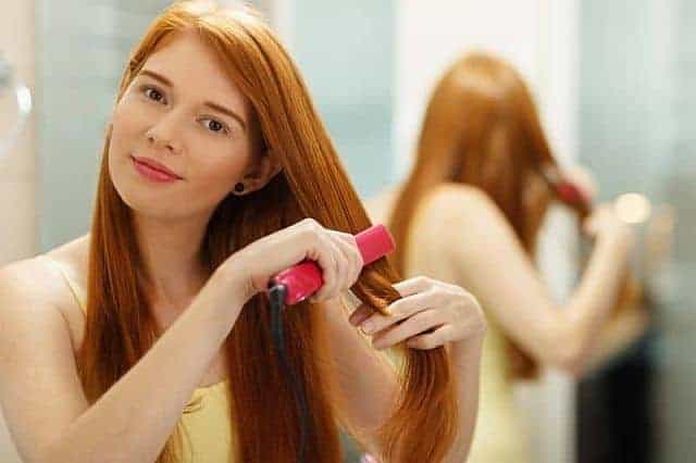 a woman flat ironing her hair after applying a leave-in conditioner