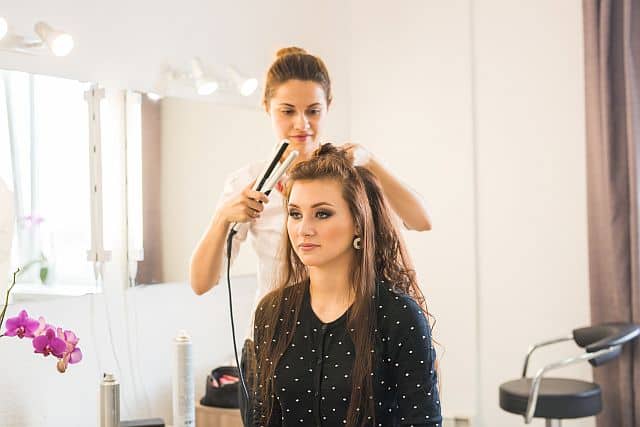 hair stylist uses hair straightener and curler to style client's hair