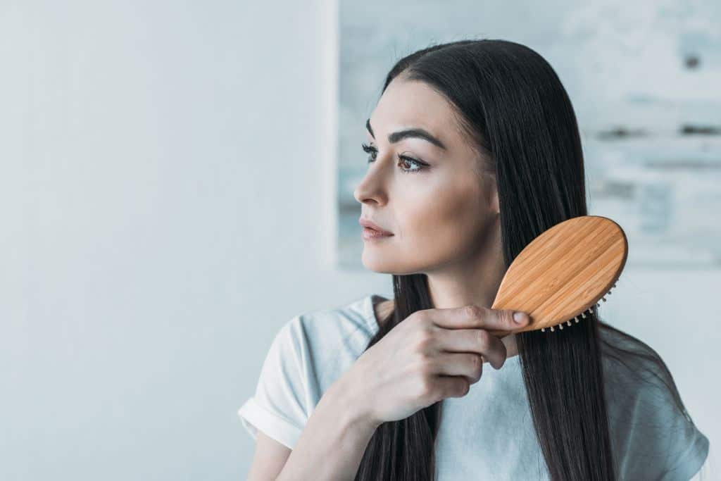 a brunette woman combs hair after applying hair building fibers 1
