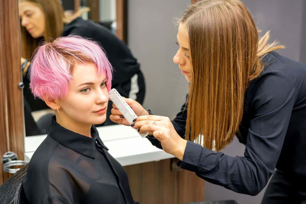 a woman with short pink hair daying and styling her hair in the salon