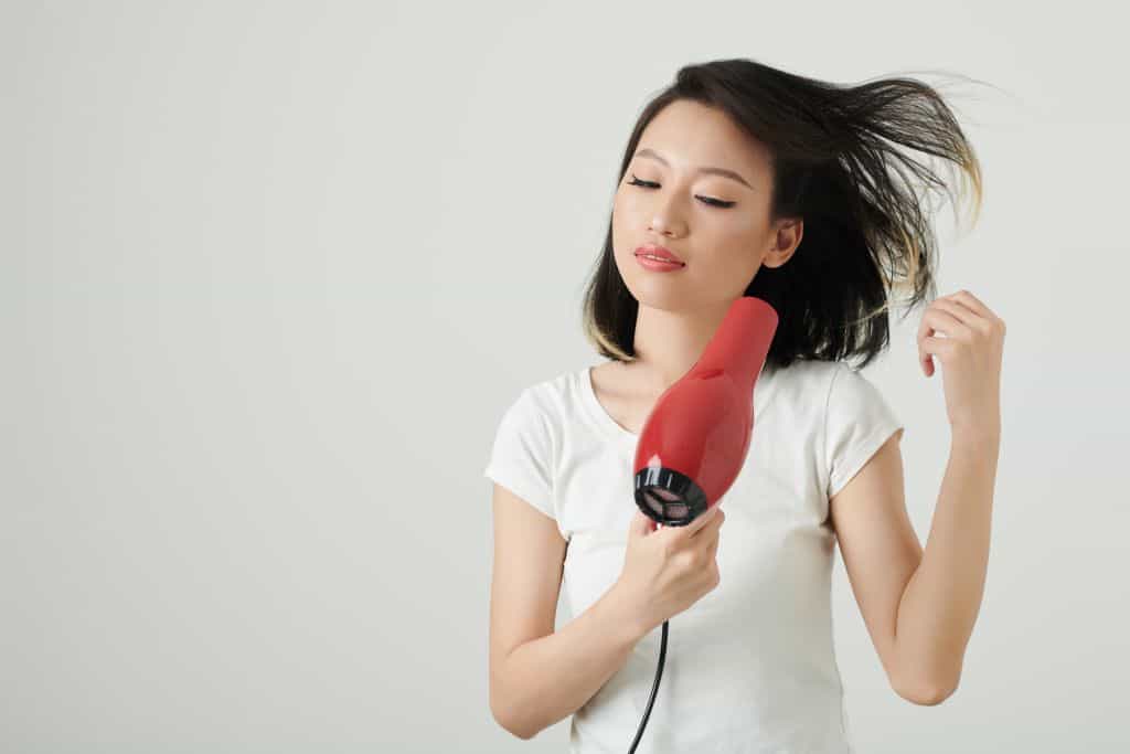 Asian woman blow drying hair with an ionic dryer