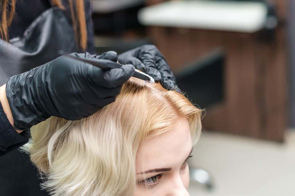 Hairdresser coloring hair roots of bleached hair