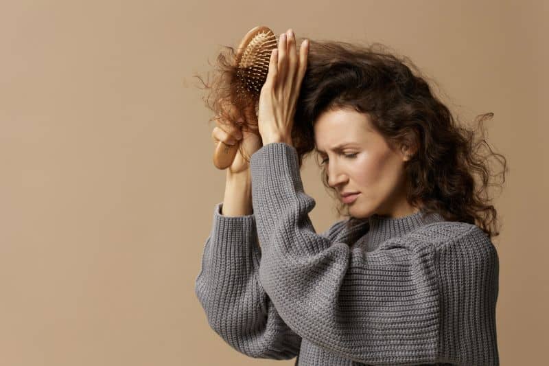unhappy curly woma in gray casual sweater brushing her frizzy hair
