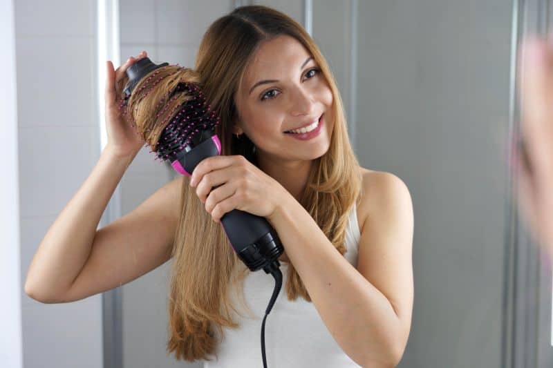 young woman using  brush hair dryer to style hair 