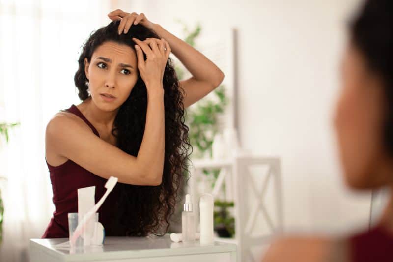 Anxious young woman looking at her hair roots and scalp in the mirror