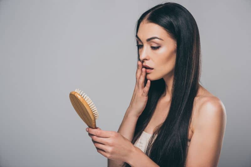 young brunette woman holding hairbrush with broken hair