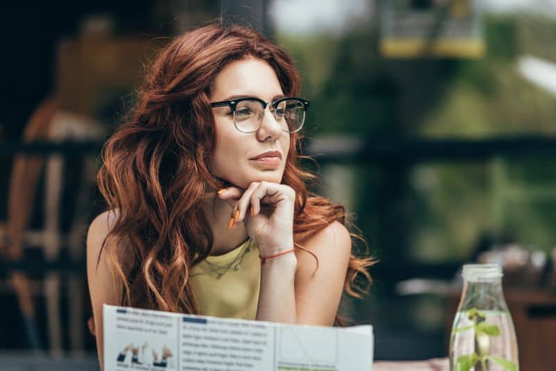 attractive redhaired woman in eyeglasses with newspaper