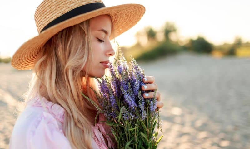 charming blonde girl in straw hat smells flowers