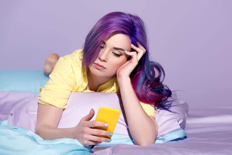 young woman with fashion hair color using smartphone in bed